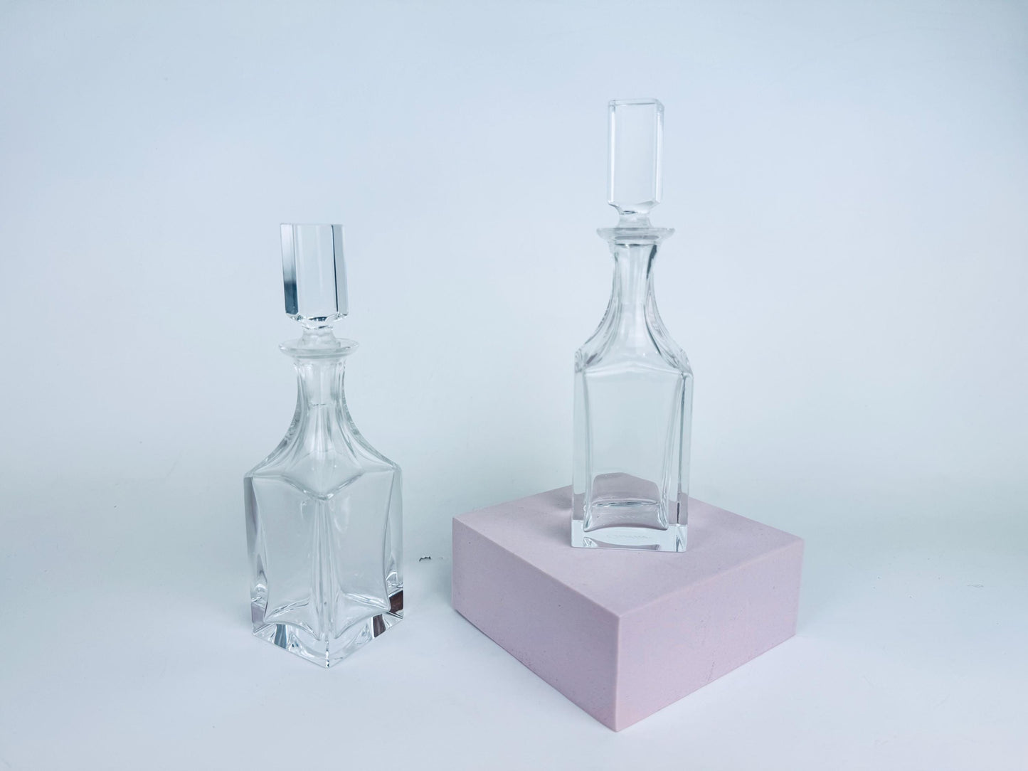 Pair of vintage Cartier clear crystal cruets with squared stoppers displayed against a red background, showing geometric form and light refraction.