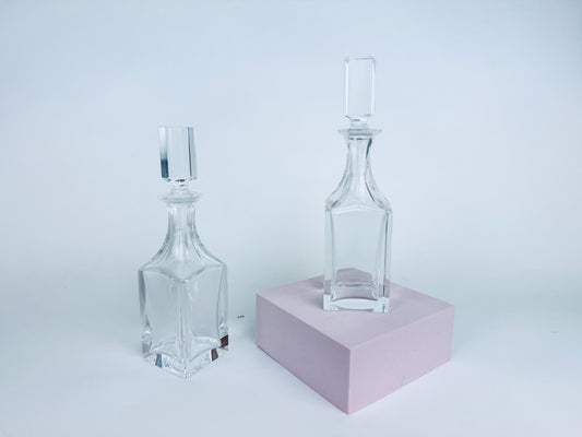 Pair of vintage Cartier clear crystal cruets with squared stoppers displayed against a red background, showing geometric form and light refraction.