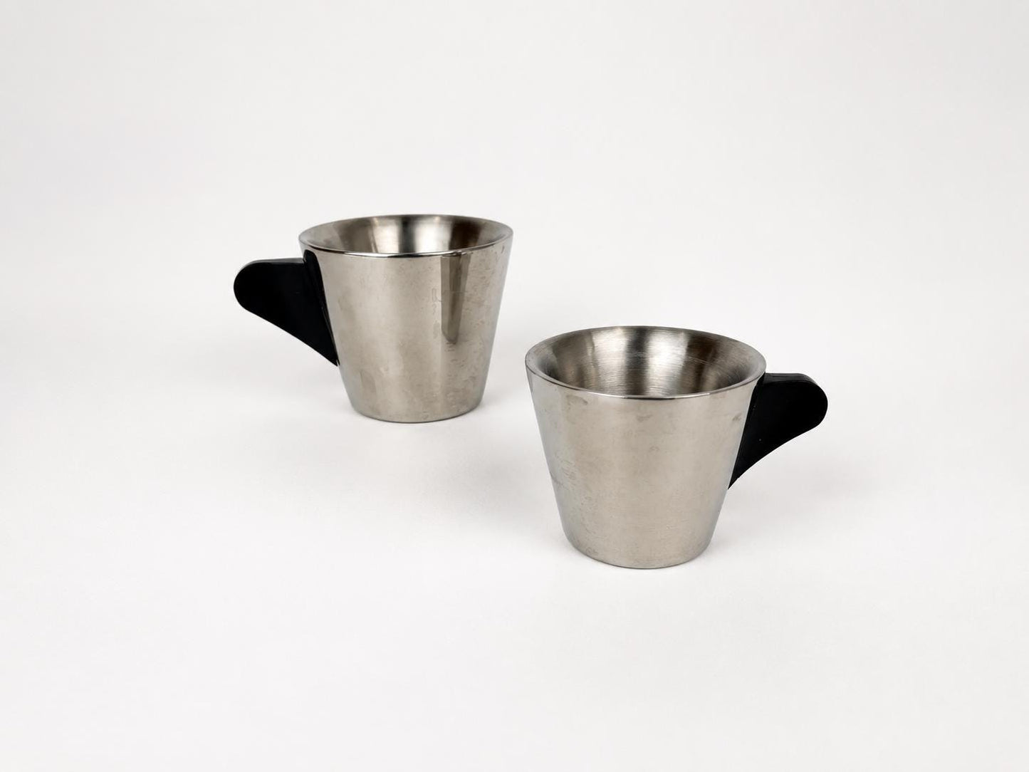 Two stainless steel coffee cups with black handles, shown on a clean white background.