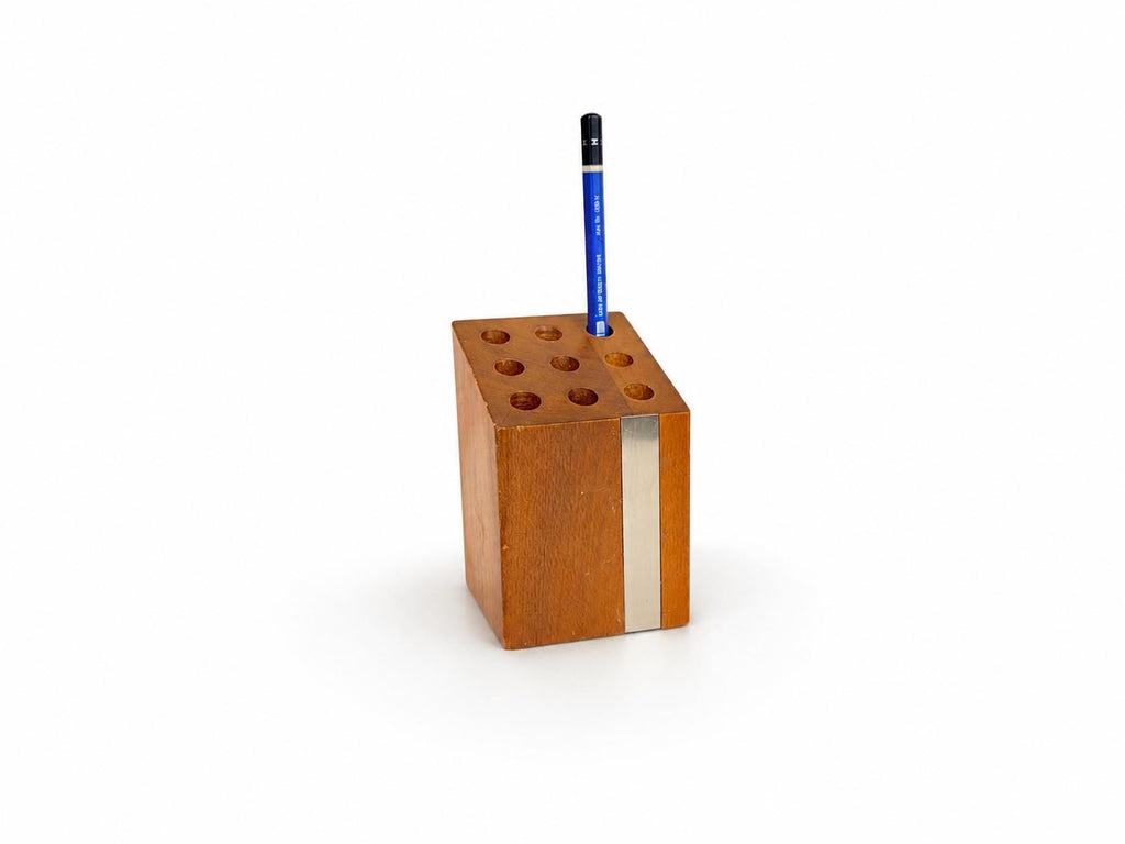 A rectangular wooden pencil holder with six circular holes, featuring a vertical silver metal stripe on the front and a blue pencil standing upright inside, set against a plain white background.