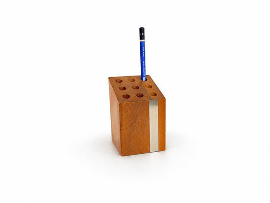 A rectangular wooden pencil holder with six circular holes, featuring a vertical silver metal stripe on the front and a blue pencil standing upright inside, set against a plain white background.